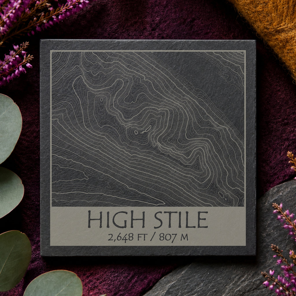 High Stile topographic slate coaster on warm wood with purple heather and green leaves