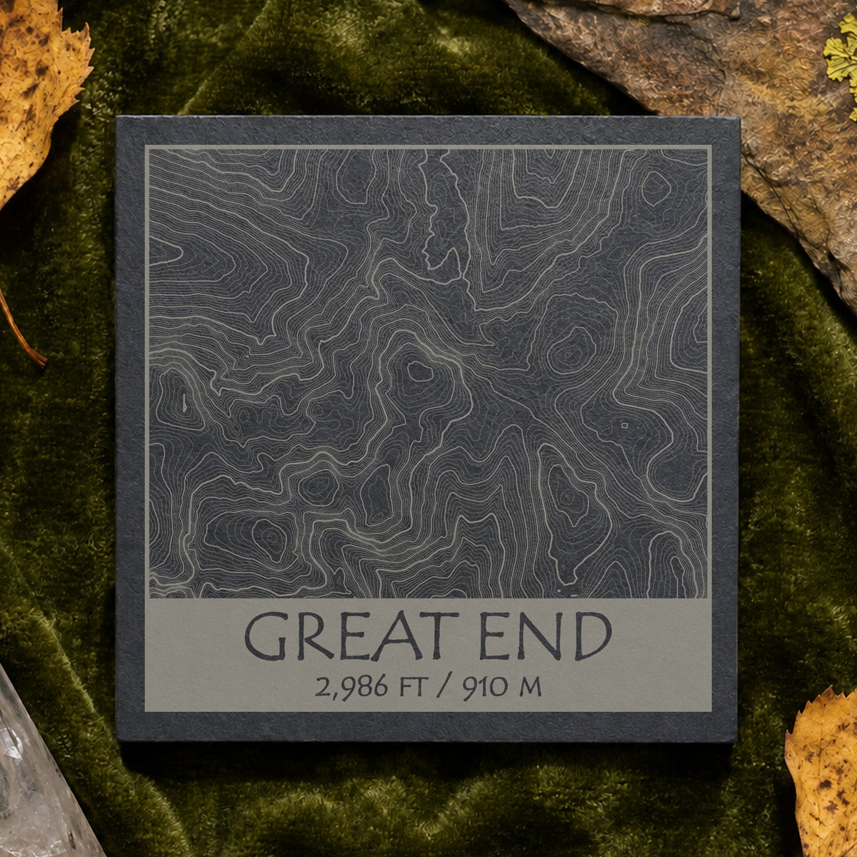 Great End topographic slate coaster on pale stone with quartz, moss and green leaves–
