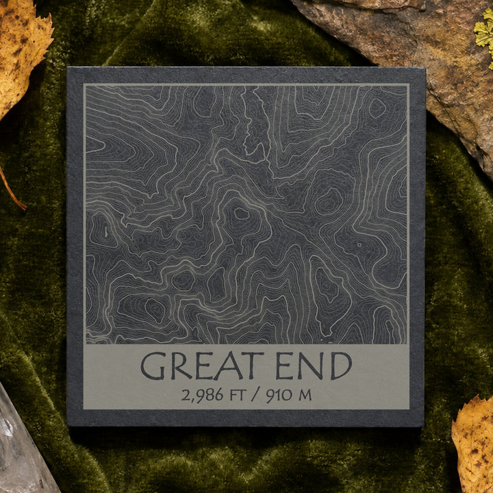 Great End topographic slate coaster on pale stone with quartz, moss and green leaves–