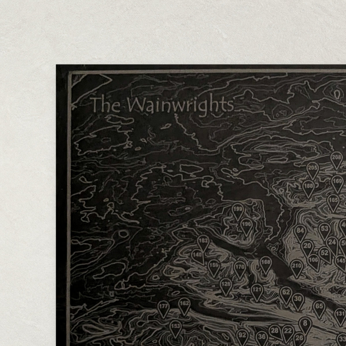 Close view of the top corner of The Wainwrights slate placemat showing the engraved title, border line and contour lines