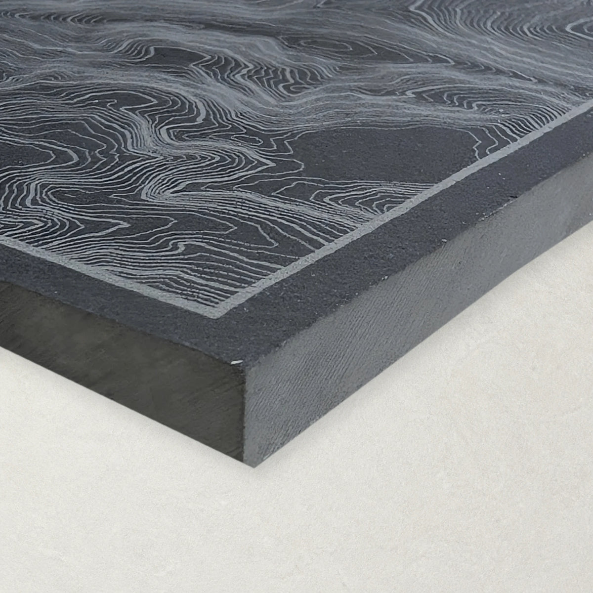 Close view of an engraved natural slate coaster showing its textured edge and corner